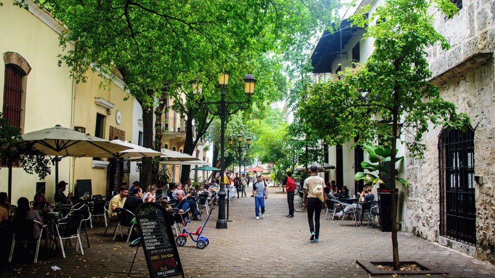 A cobblestone street lined with cafes and outdoor seating, trees, and historic buildings. 2