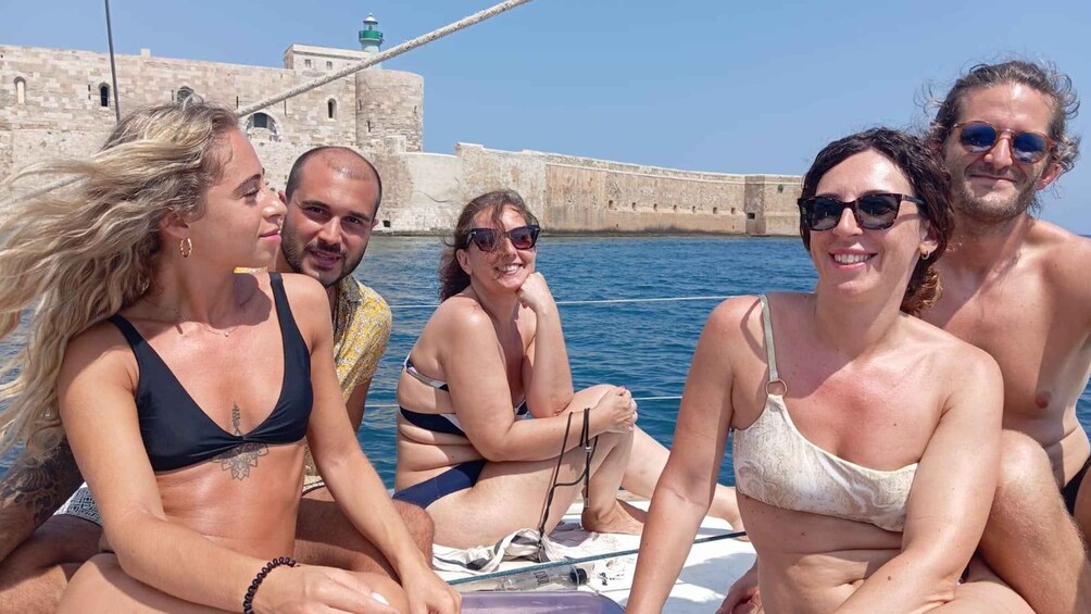 A group of people on a boat near a historic stone wall by the water. 3