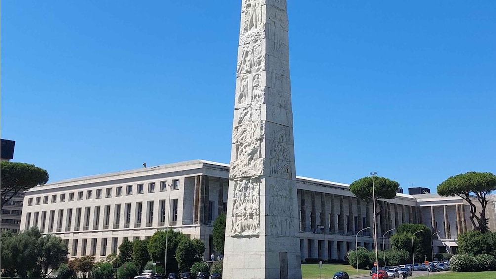A tall monument with detailed carvings, a modern building with columns, and a clear blue sky. 3