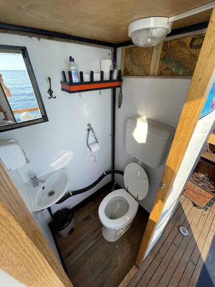 A compact bathroom with a toilet, sink, and a mirror reflecting a ship's deck. 1