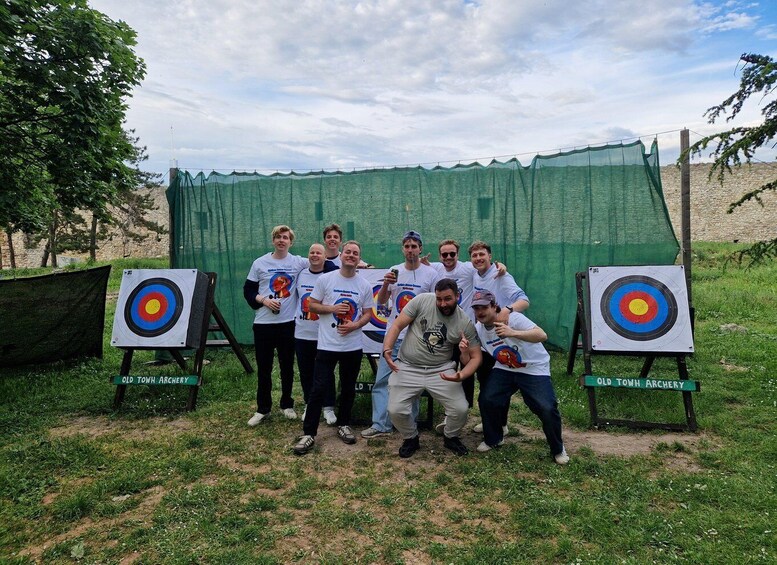 A group of people at an archery range with targets and a green backdrop. 5