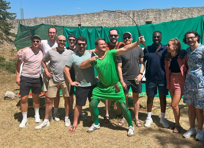 A group of people posing in front of a green backdrop with a stone wall in the background. 2