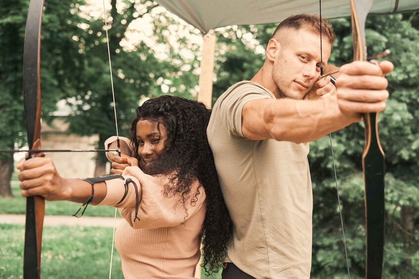 Two people archery in an outdoor setting. 1