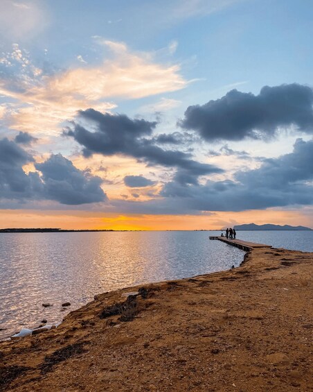 A sunset over a calm body of water with a rocky shoreline and a pier extending into the water. 2