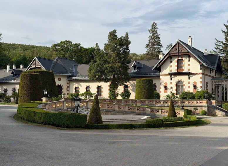 A large, historic building with a symmetrical facade, a central entrance, and a well-maintained garden with hedges and a fountain. 4