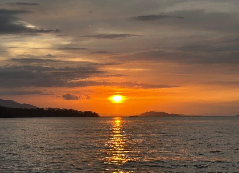 A sunset over a calm sea with a silhouette of a landmass in the distance. 2
