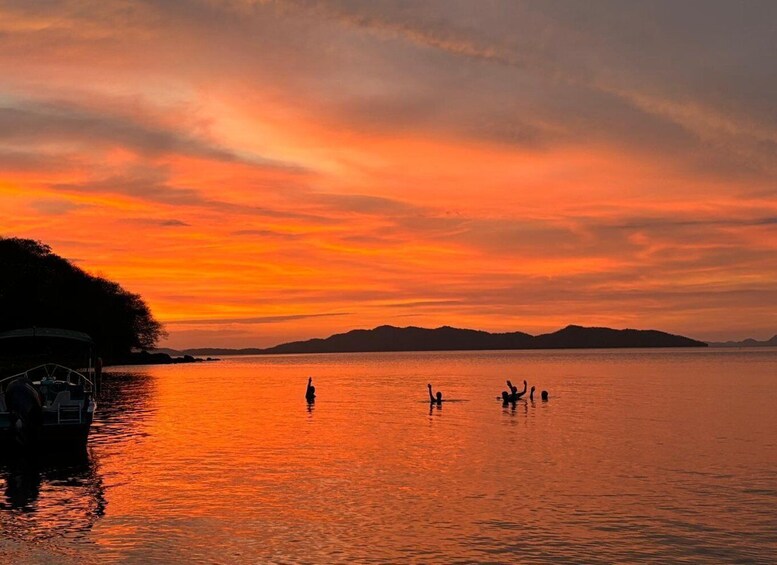 A sunset over a calm body of water with silhouettes of people and a boat. 3