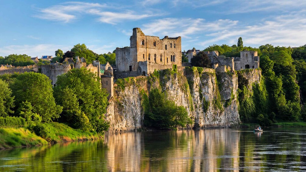 A historic castle on a cliff overlooking a calm river, surrounded by lush greenery. 5