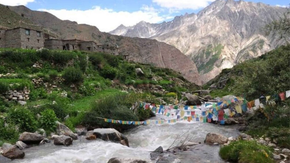 A river flowing through a mountainous valley with traditional buildings and colorful prayer flags. 2