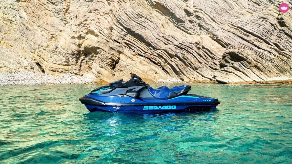 A blue Sea-Doo GTX jet ski on clear turquoise water with a rocky cliff in the background. 4