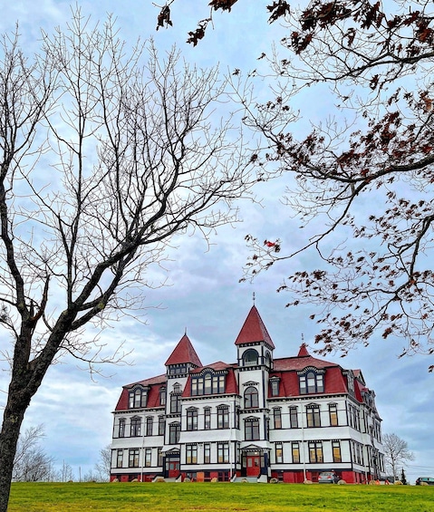 A large, historic building with a red roof and white walls, surrounded by a grassy area and trees with sparse leaves. 4
