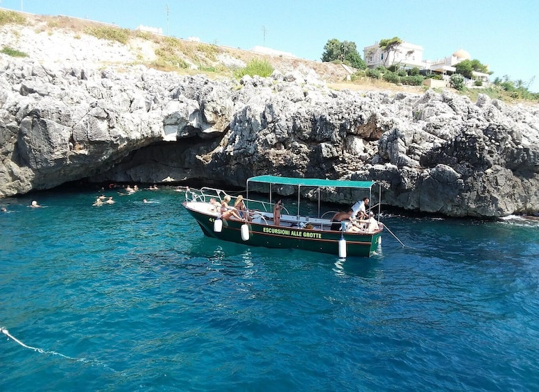 A boat named 'ESCURSONI ALLE GROTTE' on clear blue water with rocky cliffs in the background. 4