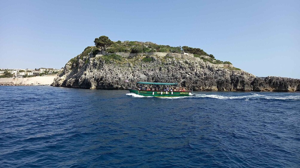 A boat with passengers traveling near a rocky island with a small settlement in the background. 5