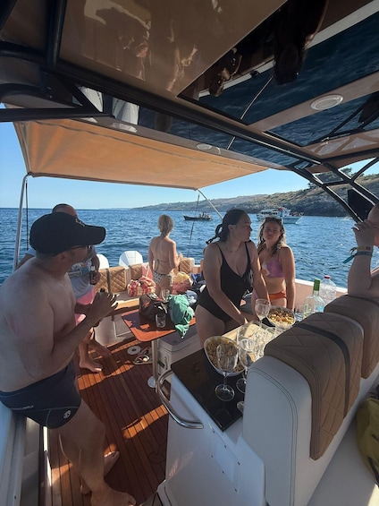 A group of people on a boat with a table set for a meal, surrounded by water and hills in the background. 1