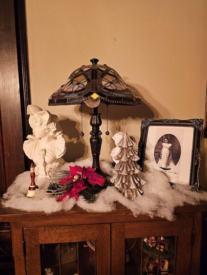 A decorative lamp, a bust, a Christmas tree, and a framed photograph on a shelf. 2
