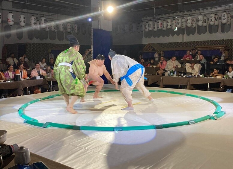 A sumo wrestling match with three wrestlers on a ring, surrounded by spectators. 1