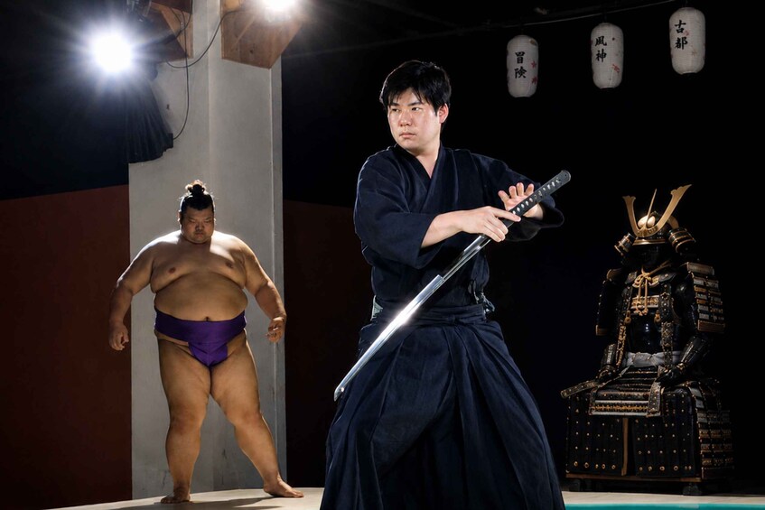 A sumo wrestler and a samurai in a dojo with a traditional Japanese warrior statue. 1
