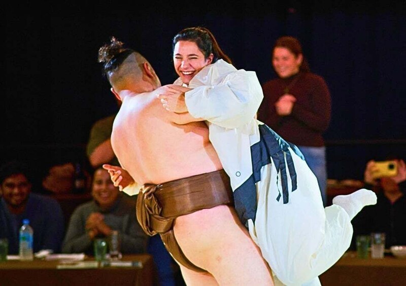 A sumo wrestler in a white and blue outfit lifting another wrestler in a brown belt. 5
