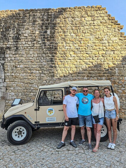 A group of people posing in front of a stone wall and a beige off-road vehicle. 3