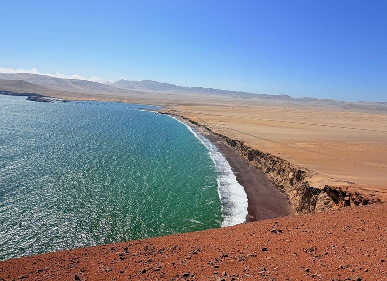 A coastal landscape with a clear blue sea, a sandy beach, and a rocky cliff. 3