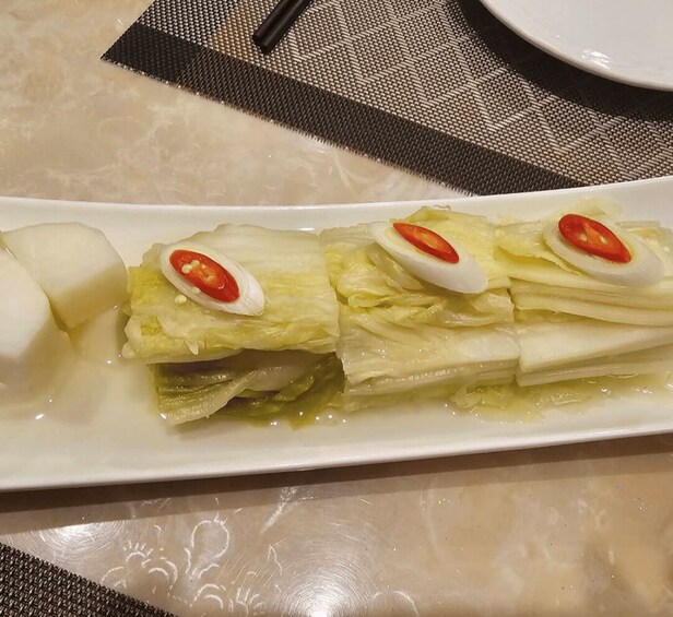 A white plate with a rolled dish of cabbage and egg slices, accompanied by a boiled egg and a slice of red chili. 2