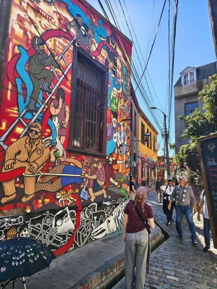 A colorful mural on a building, a cobblestone street, and a signboard with various items listed. 3