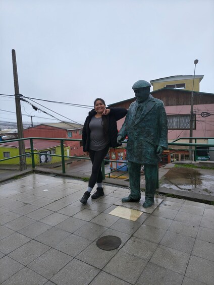 A person standing next to a statue on a wet pavement with buildings in the background. 5