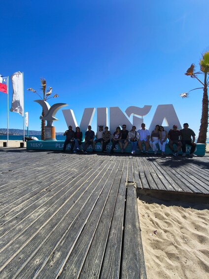 A wooden boardwalk with people sitting on a bench in front of large letters spelling 'VINCA'. 2