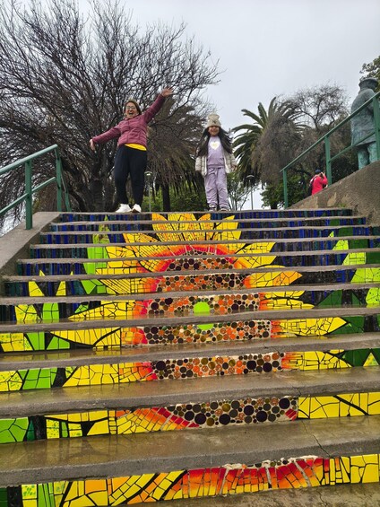 A staircase with colorful mosaic steps, surrounded by trees and a green railing. 4