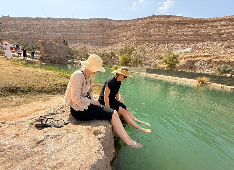 Two people sitting on a rock by a calm river with a rocky landscape in the background. 3