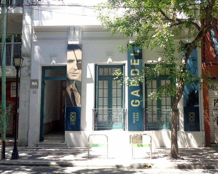 A building facade with large posters and a tree in front. 2