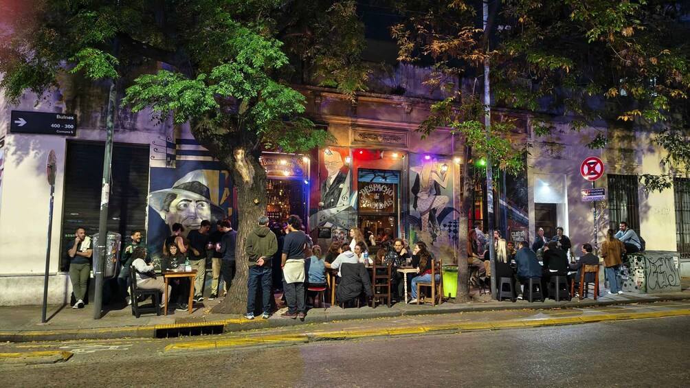 A lively street scene with people sitting and standing outside a restaurant with a mural. 3