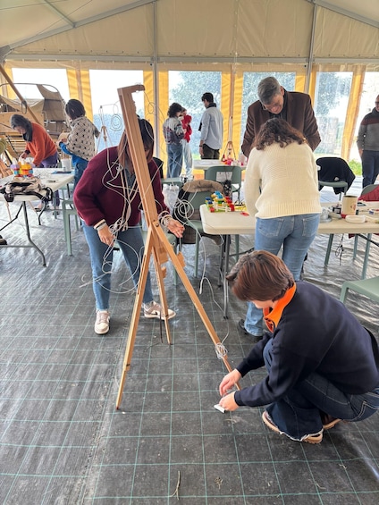 People working on an easel in a tented area with tables and chairs around. 2