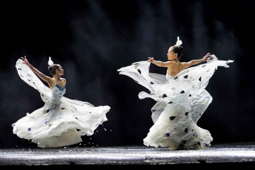 Two dancers in white costumes with feathers, performing on a stage. 1