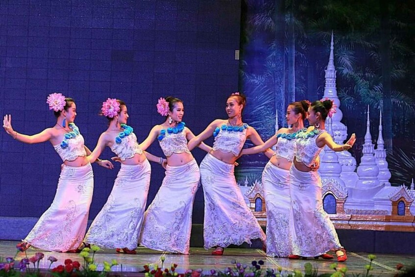 A group of dancers in white costumes with blue accents performing on a stage with a temple-like backdrop. 5