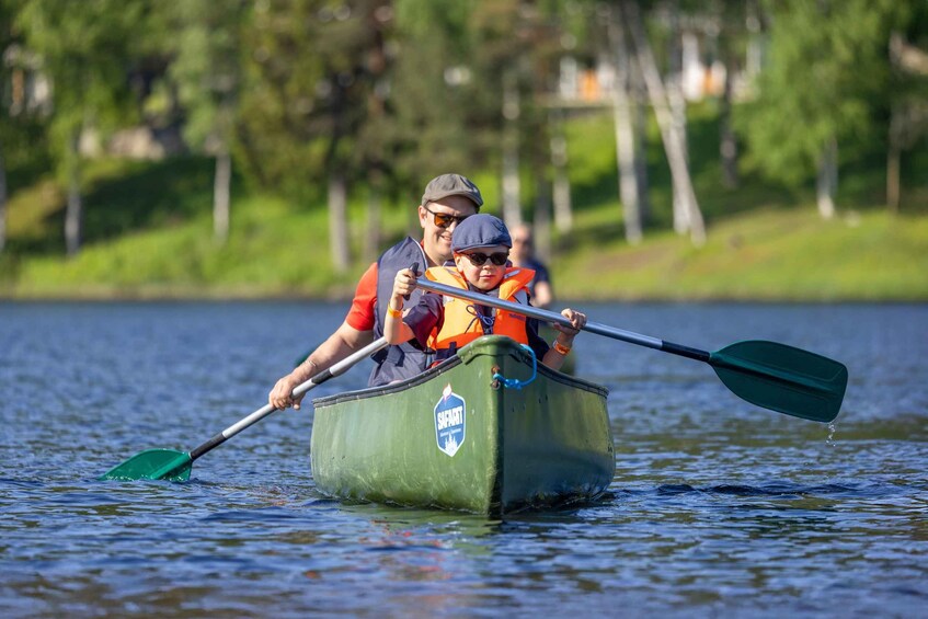 Two people in a green canoe on a calm lake, paddling with oars. 2