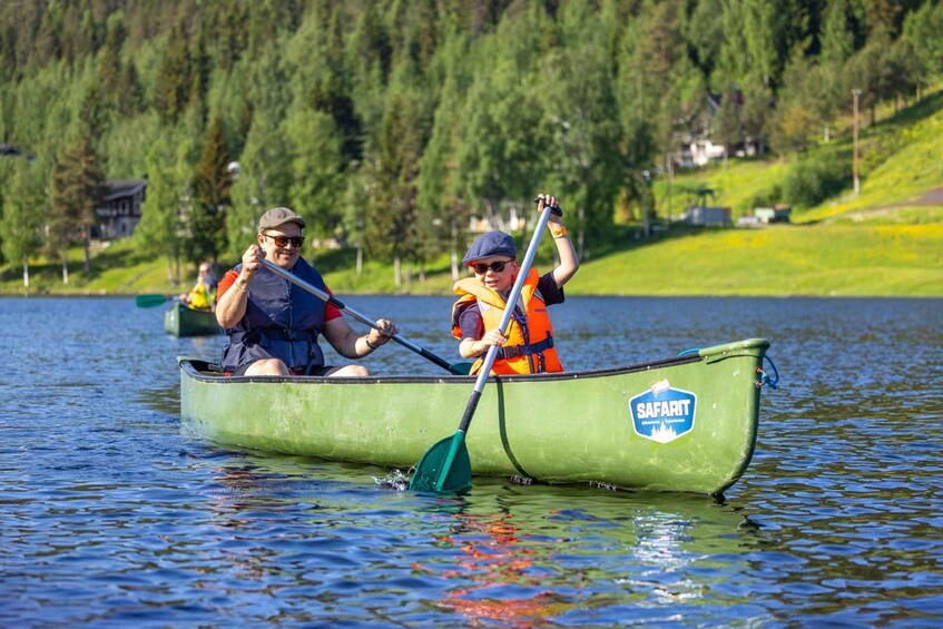 Two people in a green canoe on a lake, wearing life jackets and paddles. 1