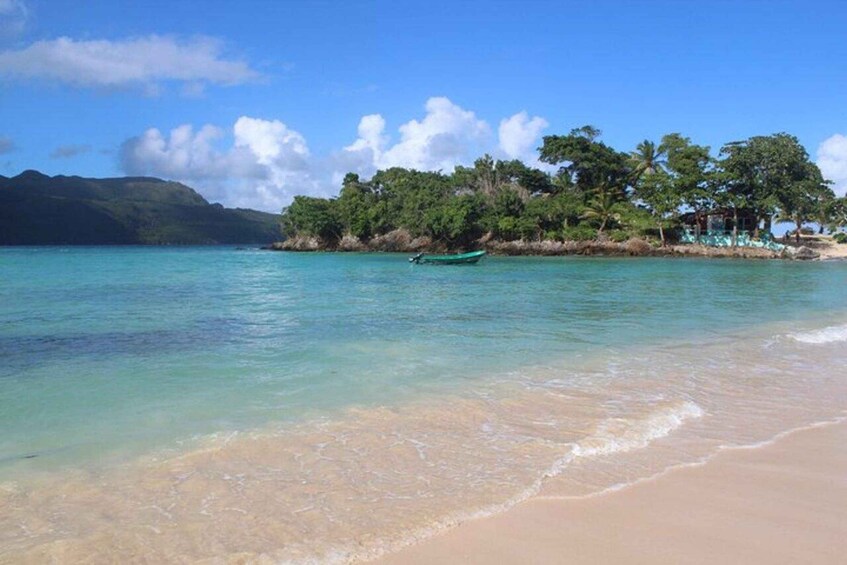 A beach with clear turquoise water, a small boat, and a forested island in the background. 2