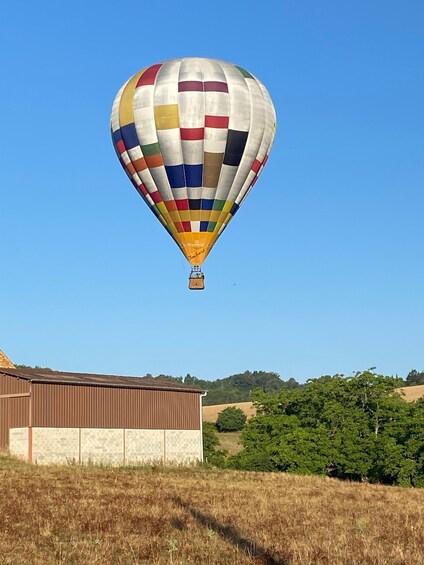 A colorful hot air balloon flying over a rural landscape with a barn and trees. 5