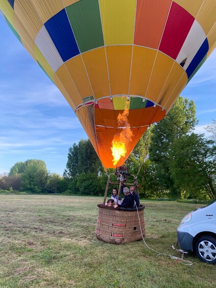 A hot air balloon with a colorful design, a basket with people, and a car parked nearby. 3