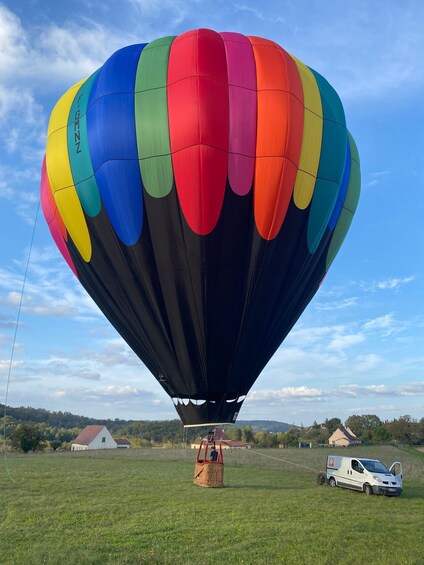 A colorful hot air balloon with a basket, a trailer, and a white van on a grassy field. 1