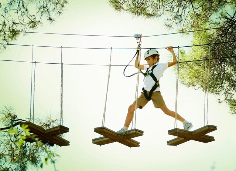 A person navigating a rope bridge suspended between wooden platforms. 1