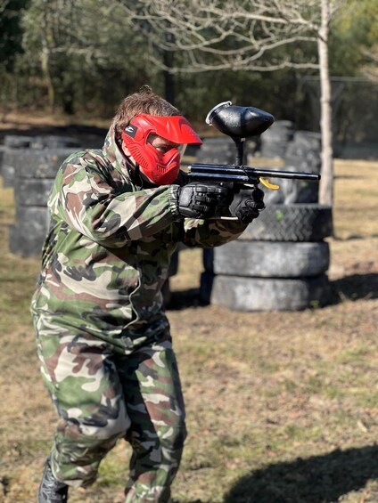 A person in camouflage paintball gear aiming a paintball gun. 1