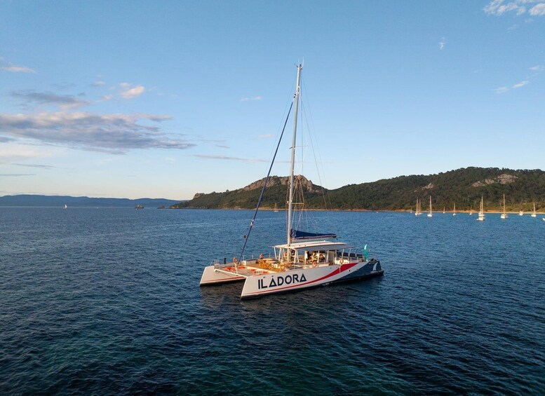 A sailboat named ILADORA on calm waters with a mountainous coastline in the background. 2