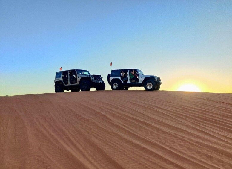 Two off-road vehicles on a sandy dune with a sunset in the background. 1