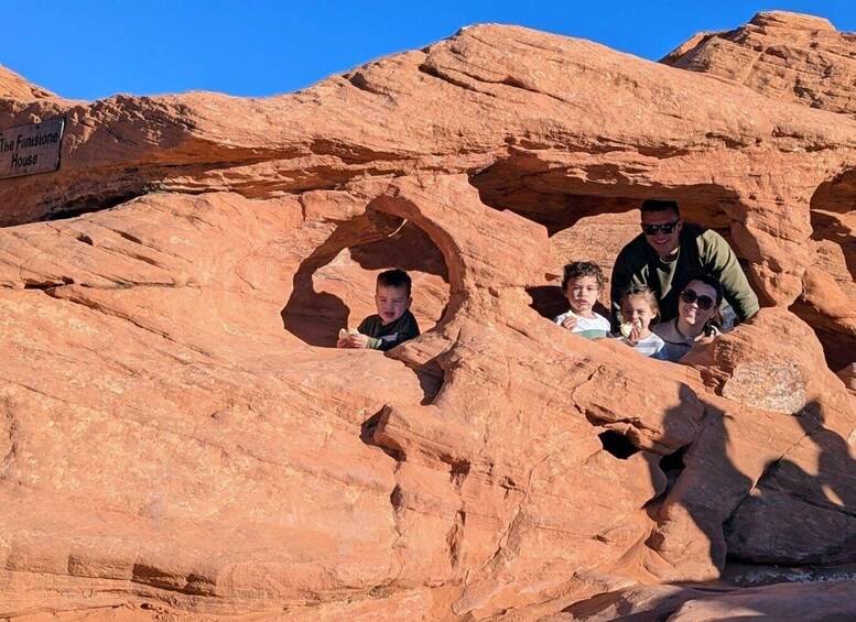 A family inside a natural rock formation with a sign reading 'The Finstone House.' 2