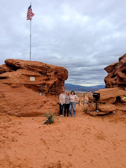 Three people standing in a desert with red rock formations and an American flag. 3