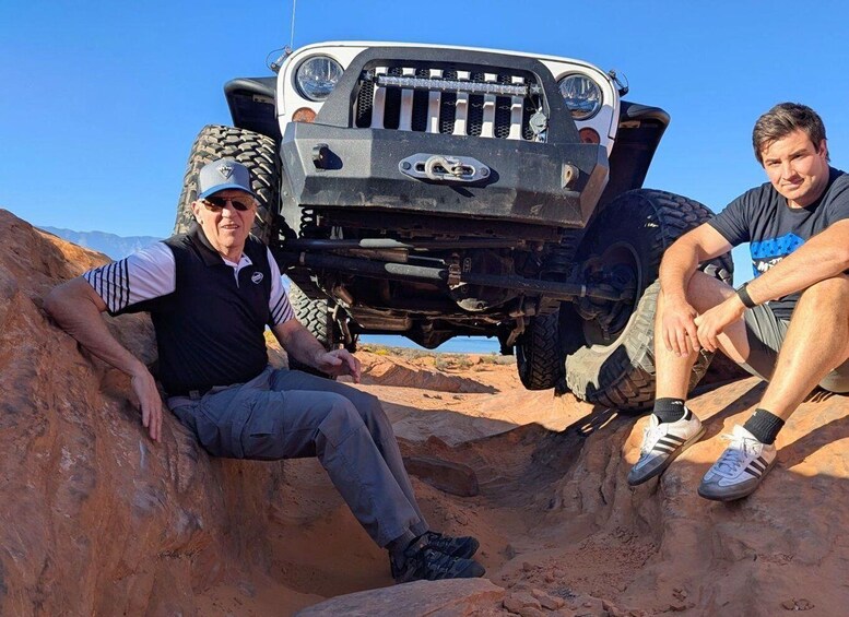 Two people sitting on a rocky terrain with a four-wheeled vehicle in the background. 4