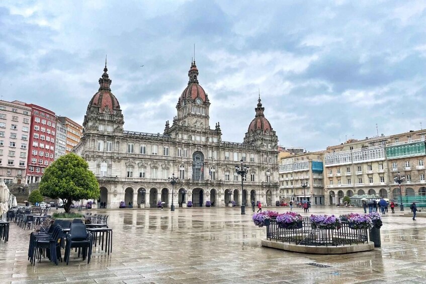 A historic building with two domes, a plaza with chairs and flowers, and modern buildings in the background. 4