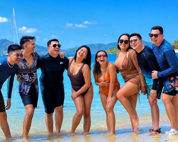 A group of people on a beach with clear blue water and a distant bridge. 3